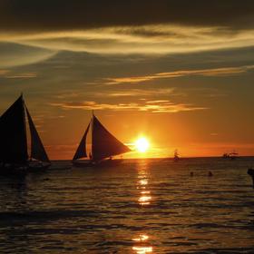 海边落日，一个人在拍照远处的帆船