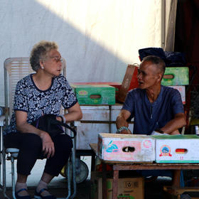 市场内，两位老人坐在摊位后面聊天，清晨的阳光洒在身...