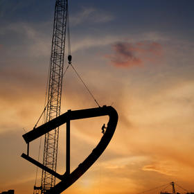 《攀登》体育馆建设工地，在上升中巨大的三角铁环上，...