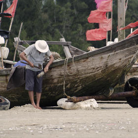 一个老渔民正在维修他那有点破旧的船，即使破旧，但他...