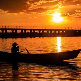 夕阳下，松花江畔，一位妇划船打渔