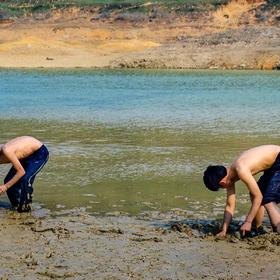 烈日下，光着膀子的两个小男孩在河里专心的寻找田螺，...