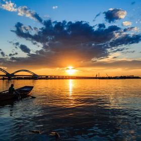 夕阳西下，松花江上，一位妇女找船打渔，...