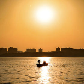湖边落日，一艘小船在整理网，等到船到太阳倒影光柱中...