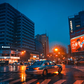 取景：闹市区的十字路口，天还没完全黑，但是因为下雨...