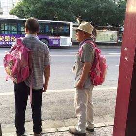 送孩子上学的路上，看见两位老人背着粉色的书包，胸前...